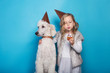 Little beautiful girl with dog celebrate birthday. Friendship. Love. Cake with candle. Studio portrait over blue background